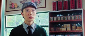 Movie still from “Ip Man 3” (2015), directed by Wilson Yip – A man wearing glasses and a hat in front of a book case; Close Up shot, Low angle
