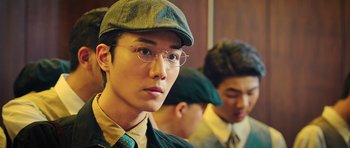 Movie still from “Ip Man 3” (2015), directed by Wilson Yip – A man with glasses and a hat is looking at the camera; Close Up shot, Over the shoulder angle