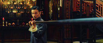 Movie still from “Ip Man 3” (2015), directed by Wilson Yip – A man holding a baseball bat while standing in front of a building; Medium shot, Low angle