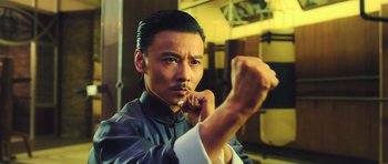 Movie still from “Ip Man 3” (2015), directed by Wilson Yip – A man in a black and white shirt is holding his fist up; Close Up shot, Low angle