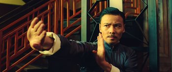 Movie still from “Ip Man 3” (2015), directed by Wilson Yip – A man in a black and white shirt is holding his hand up to his face; Close Up shot, Low angle