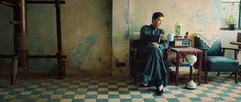 Movie still from “Ip Man 3” (2015), directed by Wilson Yip – A man sitting on a chair with a cup of coffee; Medium shot, Low angle
