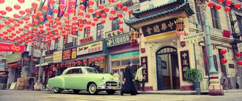 Movie still from “Ip Man 4: The Finale” (2019), directed by Wilson Yip – A man walking down the street with a green car; Extreme Wide shot, High angle