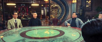 Movie still from “Ip Man 4: The Finale” (2019), directed by Wilson Yip – Two men sitting at a table in front of a clock; Medium shot, Over the shoulder angle