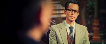 Movie still from “Ip Man 4: The Finale” (2019), directed by Wilson Yip – A man wearing a suit and tie sitting in a chair; Medium shot, Over the shoulder angle