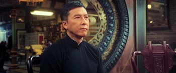 Movie still from “Ip Man 4: The Finale” (2019), directed by Wilson Yip – A man wearing a black shirt and standing in front of an ornate wall; Close Up shot, Low angle