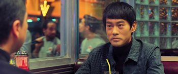 Movie still from “Ip Man 4: The Finale” (2019), directed by Wilson Yip – A man sitting at a table with a drink in front of him; Close Up shot, Over the shoulder angle