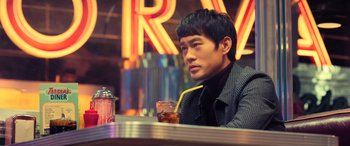 Movie still from “Ip Man 4: The Finale” (2019), directed by Wilson Yip – A man sitting at a table in front of a neon sign; Medium shot, Over the shoulder angle
