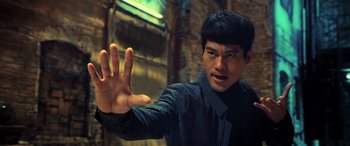 Movie still from “Ip Man 4: The Finale” (2019), directed by Wilson Yip – A young man holding his hand up in the air in front of a brick wall; Close Up shot, Low angle