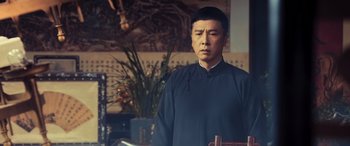Movie still from “Ip Man 4: The Finale” (2019), directed by Wilson Yip – A man standing in front of a table with a cross; Medium shot, Low angle