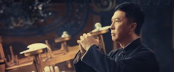 Movie still from “Ip Man 4: The Finale” (2019), directed by Wilson Yip – A man in a black suit is praying; Close Up shot, Over the shoulder angle