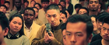 Movie still from “Ip Man 4: The Finale” (2019), directed by Wilson Yip – A man taking a picture in front of a group of people; Medium shot, Over the shoulder angle