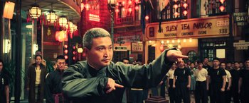 Movie still from “Ip Man 4: The Finale” (2019), directed by Wilson Yip – A man pointing to the side while standing on a street; Medium shot, Low angle