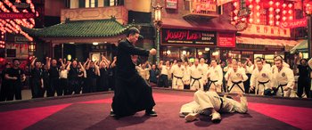 Movie still from “Ip Man 4: The Finale” (2019), directed by Wilson Yip – A man in a black robe and a white robe fighting in front of an audience; Wide shot, High angle