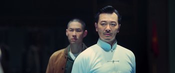 Movie still from “Ip Man 4: The Finale” (2019), directed by Wilson Yip – Two men standing next to each other in front of a wall; Medium shot, Low angle