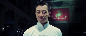 Movie still from “Ip Man 4: The Finale” (2019), directed by Wilson Yip – A man in a white shirt is standing in front of a flag; Close Up shot, Low angle