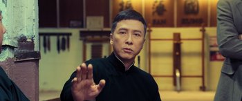 Movie still from “Ip Man 4: The Finale” (2019), directed by Wilson Yip – A man in a black shirt is holding out his hand; Close Up shot, Over the shoulder angle