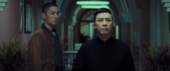 Movie still from “Ip Man 4: The Finale” (2019), directed by Wilson Yip – A man standing next to another man in a room; Medium shot, Low angle