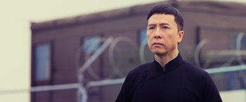 Movie still from “Ip Man 4: The Finale” (2019), directed by Wilson Yip – A man wearing a black shirt and standing in front of a building; Close Up shot, Over the shoulder angle