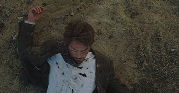 Movie still from “Iron Man” (2008), directed by Jon Favreau – A man is laying on the ground covered in blood; Medium shot, Overhead angle
