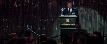 Movie still from “Iron Man” (2008), directed by Jon Favreau – A man standing at a podium in front of a crowd; Medium shot, Over the shoulder angle