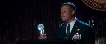 Movie still from “Iron Man” (2008), directed by Jon Favreau – A man holding a microphone in front of a microphone stand; Close Up shot, Low angle