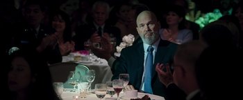 Movie still from “Iron Man” (2008), directed by Jon Favreau – A man sitting at a dinner table with his hands clapping; Medium shot, Over the shoulder angle