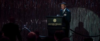 Movie still from “Iron Man” (2008), directed by Jon Favreau – A man standing at a lectern in front of a crowd; Medium shot, Over the shoulder angle