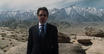 Movie still from “Iron Man” (2008), directed by Jon Favreau – A man in a suit and tie standing in front of mountains; Medium shot, Low angle