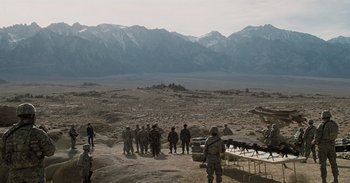 Movie still from “Iron Man” (2008), directed by Jon Favreau – A group of men standing on top of a dirt field; Extreme Wide shot, High angle