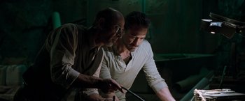 Movie still from “Iron Man” (2008), directed by Jon Favreau – Two men looking at something in a dark room; Medium shot, Low angle