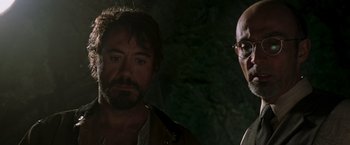Movie still from “Iron Man” (2008), directed by Jon Favreau – A man standing next to another man wearing glasses; Close Up shot, Low angle