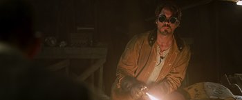 Movie still from “Iron Man” (2008), directed by Jon Favreau – A man in a brown jacket and sunglasses is holding a light; Medium shot, Over the shoulder angle