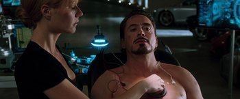 Movie still from “Iron Man” (2008), directed by Jon Favreau – A man sitting next to a woman in a chair; Medium shot, Over the shoulder angle