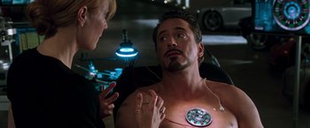 Movie still from “Iron Man” (2008), directed by Jon Favreau – A man with an iron man chest tattoo is being examined by a woman; Close Up shot, Over the shoulder angle