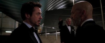 Movie still from “Iron Man” (2008), directed by Jon Favreau – Two men in tuxedos talking to each other in a building; Close Up shot, Over the shoulder angle