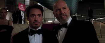 Movie still from “Iron Man” (2008), directed by Jon Favreau – Two men in tuxedos pose for a picture; Close Up shot, Low angle