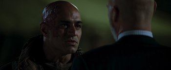 Movie still from “Iron Man” (2008), directed by Jon Favreau – A man with a shaved head and a bald head is talking to another man in a suit; Close Up shot, Over the shoulder angle