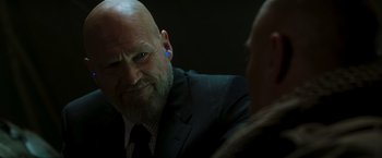 Movie still from “Iron Man” (2008), directed by Jon Favreau – A bald man with a blue earring in his ear; Close Up shot, Over the shoulder angle