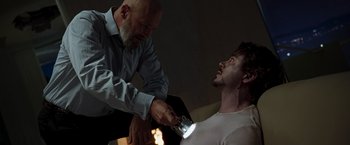 Movie still from “Iron Man” (2008), directed by Jon Favreau – A man is lighting a candle on a man's face; Medium shot, Over the shoulder angle