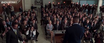 Movie still from “Iron Man” (2008), directed by Jon Favreau – A group of people sitting in front of an audience; Wide shot, High angle