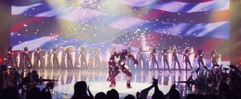 Movie still from “Iron Man 2” (2010), directed by Jon Favreau – A man dressed as iron man performs on a stage; Wide shot, Low angle