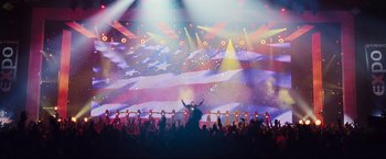 Movie still from “Iron Man 2” (2010), directed by Jon Favreau – A crowd of people in front of an american flag lit up screen; Extreme Wide shot, Low angle