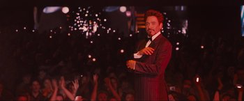 Movie still from “Iron Man 2” (2010), directed by Jon Favreau – A man wearing a suit and tie standing in front of a crowd of onlookers; Medium shot, Low angle