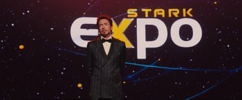 Movie still from “Iron Man 2” (2010), directed by Jon Favreau – A man standing in front of an expo sign; Medium shot, Low angle