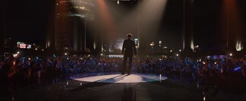 Movie still from “Iron Man 2” (2010), directed by Jon Favreau – A man standing on a stage in front of an audience; Wide shot, Low angle