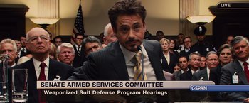 Movie still from “Iron Man 2” (2010), directed by Jon Favreau – A group of people in a room with a man in a suit; Close Up shot, Over the shoulder angle