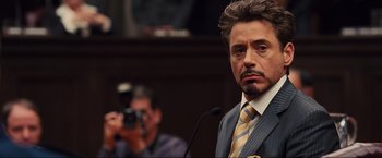 Movie still from “Iron Man 2” (2010), directed by Jon Favreau – A man in a suit and tie standing in front of a camera; Close Up shot, Over the shoulder angle