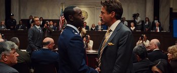 Movie still from “Iron Man 2” (2010), directed by Jon Favreau – Two men in suits shaking hands in front of a crowd; Medium shot, Over the shoulder angle