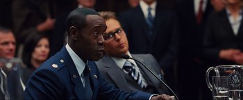 Movie still from “Iron Man 2” (2010), directed by Jon Favreau – Two men in suits and ties are sitting in front of microphones; Close Up shot, Over the shoulder angle